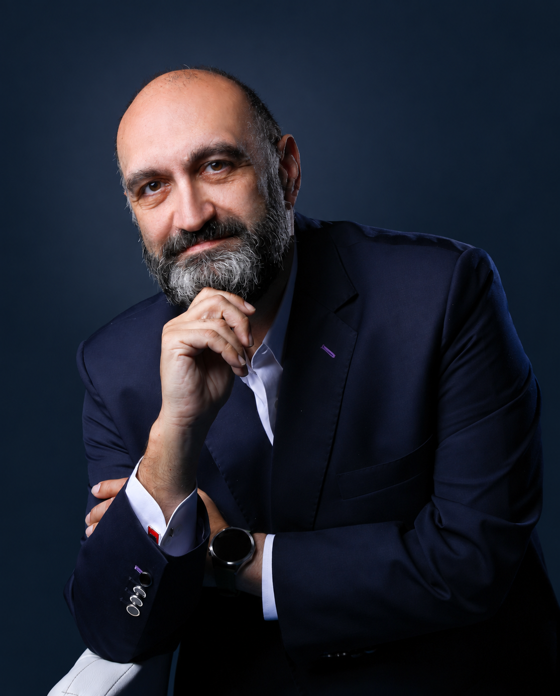 Malek Mroueh resting his hand beneath his chin, wearing a navy jacket